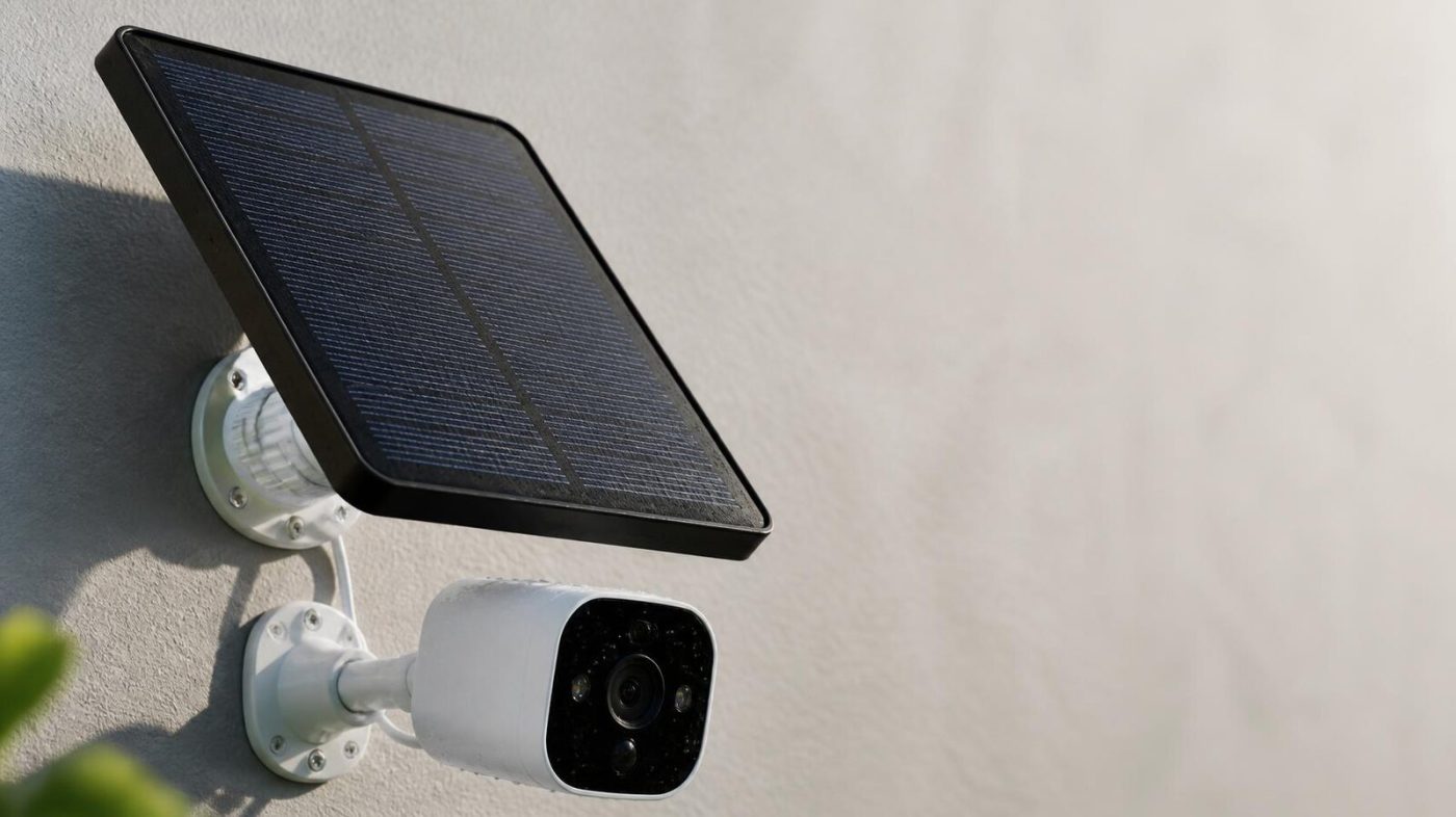 Close-up of a solar panel connected to a white outdoor security camera on a sunlit wall